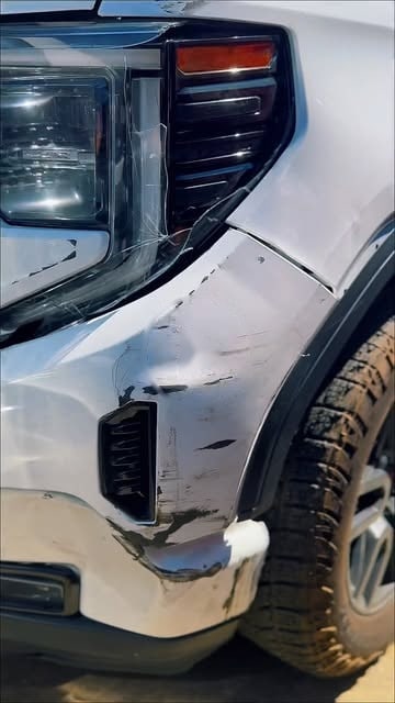 A white GMC Sierra with front fender damage, before repair
